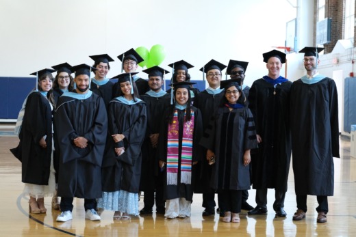 Group of MEITE graduate students pose in cap and gown at graduation ceremony.