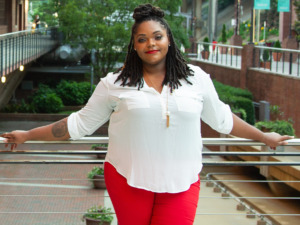 Brittanie Howard is leaning against a railing. She is wearing red pants and a white shirt.