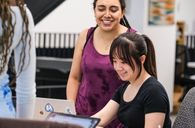 Two MEITE program students collaborating while looking at a laptop.