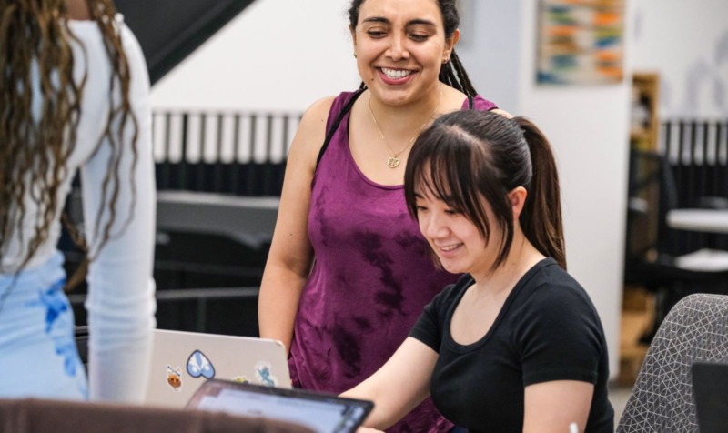 Two MEITE program students collaborating while looking at a laptop.