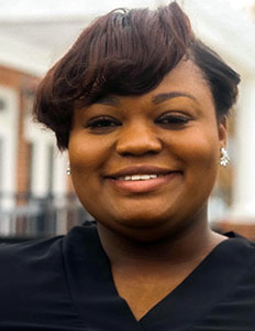 Portrait of Camryn Anderson. Camryn is a black woman with straight brown hair wearing a black shirt.