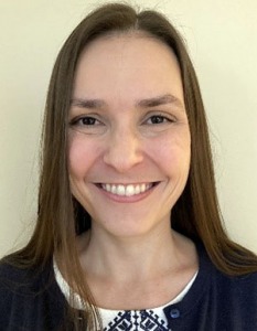 Portrait of Leah Fulkerson. Leah is a white woman with straight brown hair. She is wearing a white shirt and blue cardigan and smiling at the camera.