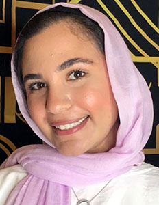 Portrait of Iman Ibrahim. Iman is a woman with light skin and dark hair. She is wearing a pink headscarf and smiling at the camera.
