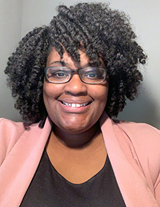 Portrait of Yalanda Lawson. Yalanda is a dark skinned woman with curly black hair. She is wearing a black shirt, pink blazer and glasses and is smiling at the camera.