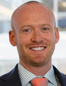 Portrait of Ryan Welsh. Ryan is a white man with no hair and a short beard. He is wearing a black suit and smiling.