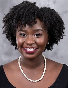 Portrait of Bryanna Williams. Bryanna is a black woman with curly black hair. She is wearing a black shirt, pearl necklace, and smiling.