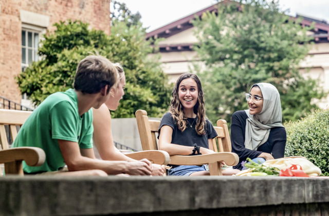 Four students sitting on a bench in front of UNC's South Building