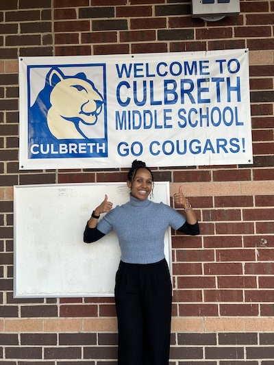 Selah Bekele-Piper standing underneath a sign that says "Welcome to Culbreth Middle School. Go Cougars."