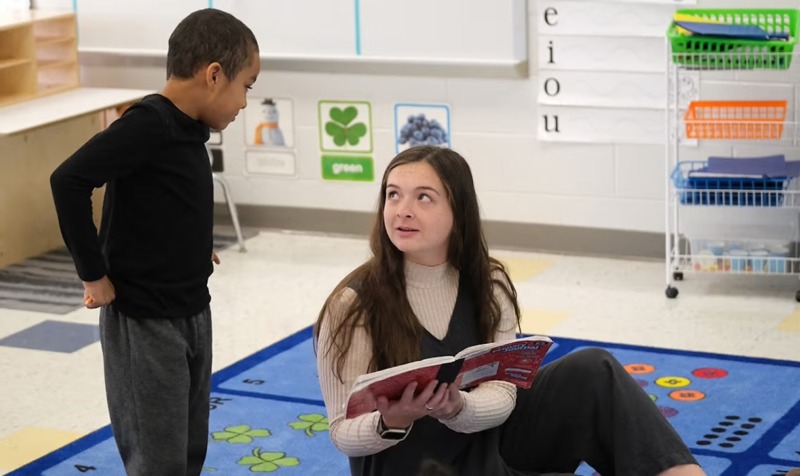 Madison Sturdivant reads to a student on a rug in her classroom