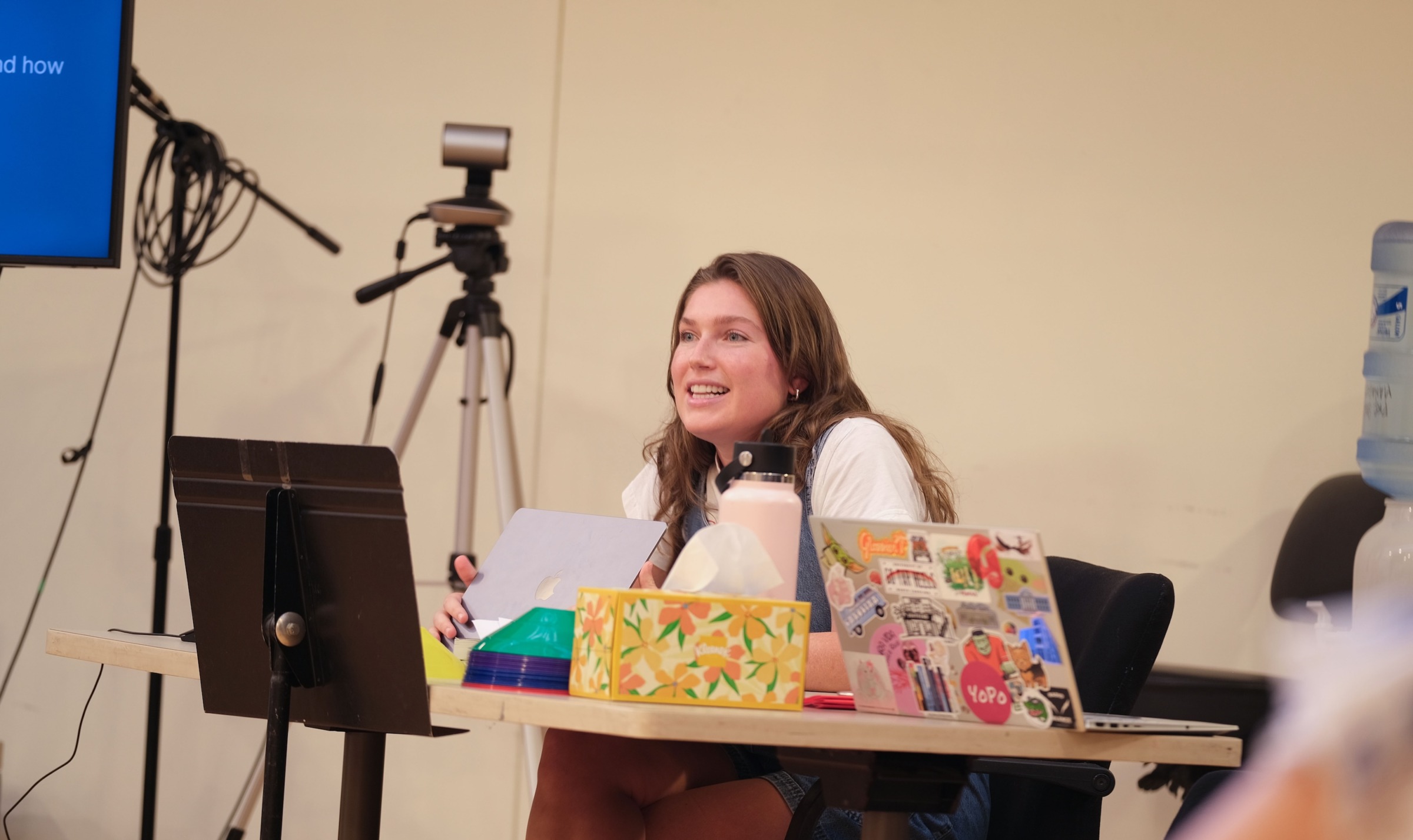 School counseling student Chloe Rhodes sits at a table with her laptop open, presenting to the cast of The Wolves about neuroscience