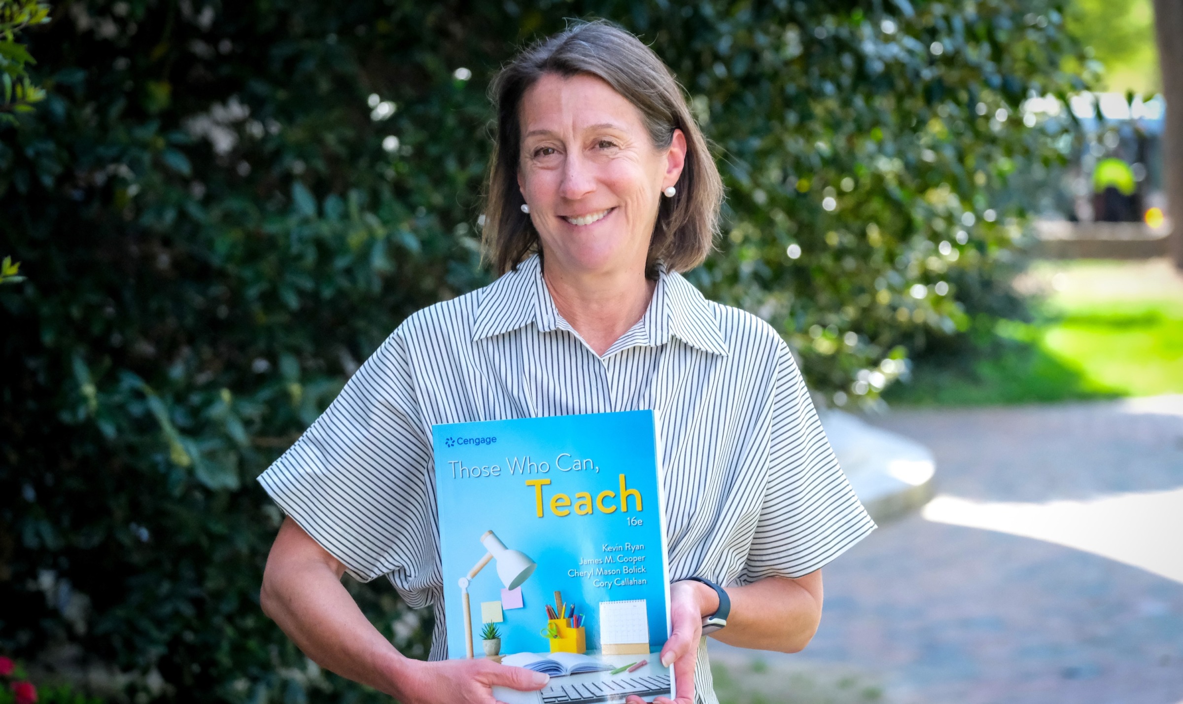 Image of Cheryl Bolick, Ph.D., standing outside of Peabody Hall, holding a copy of the textbook 