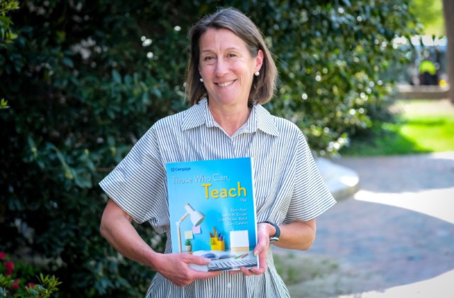 Image of Cheryl Bolick, Ph.D., standing outside of Peabody Hall, holding a copy of the textbook 