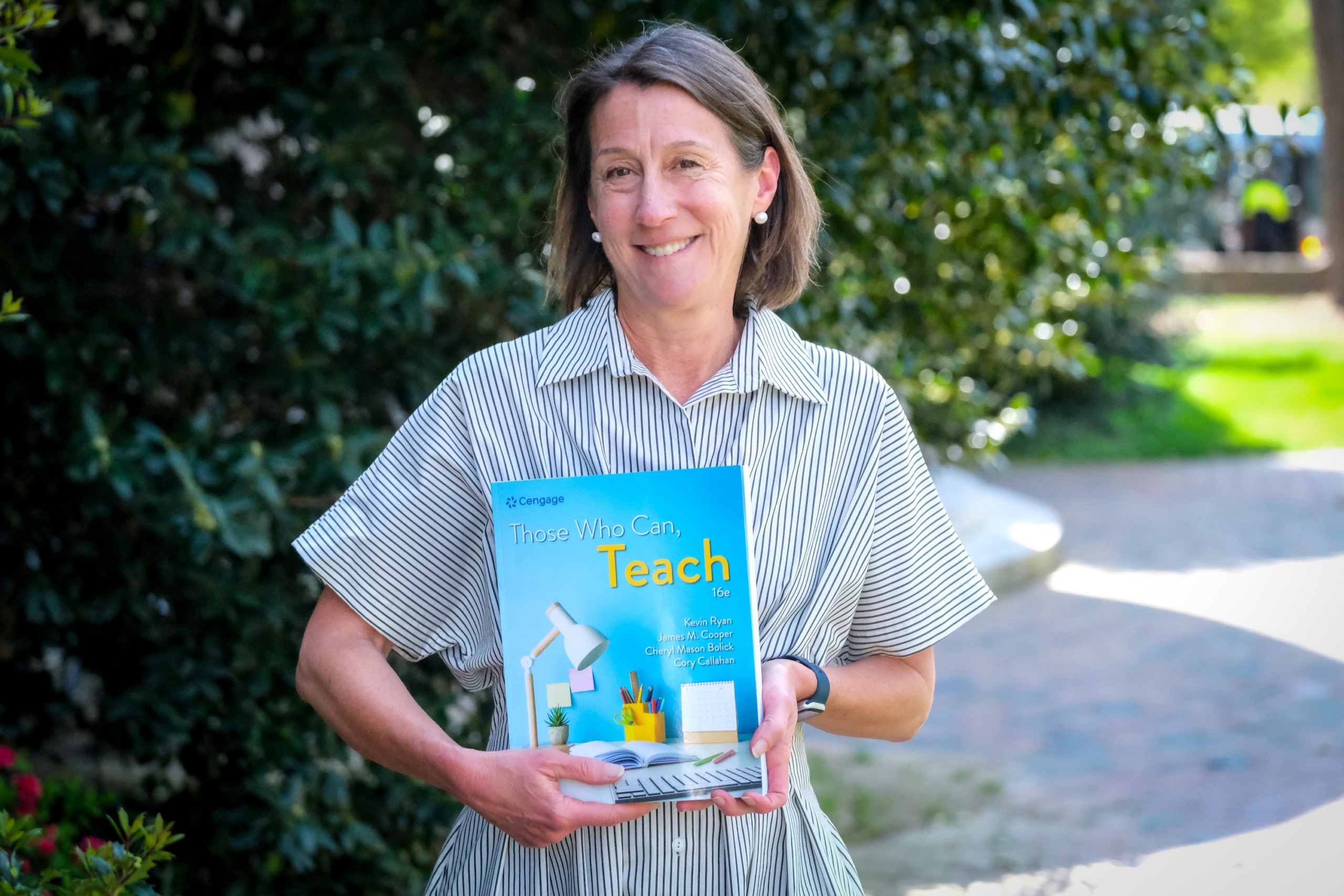 Image of Cheryl Bolick, Ph.D., standing outside of Peabody Hall, holding a copy of the textbook 