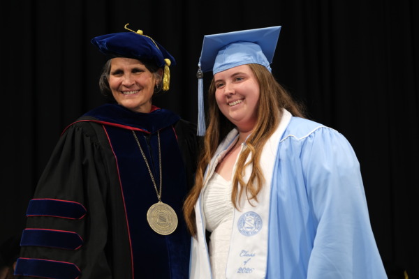 Avery Humphries, wearing Carolina Blue graduation regalia, smiles beside Jill V. Hamm, Ph.D., UNC School of Education dean, in academic regalia during the School's 2026 graduation celebration.