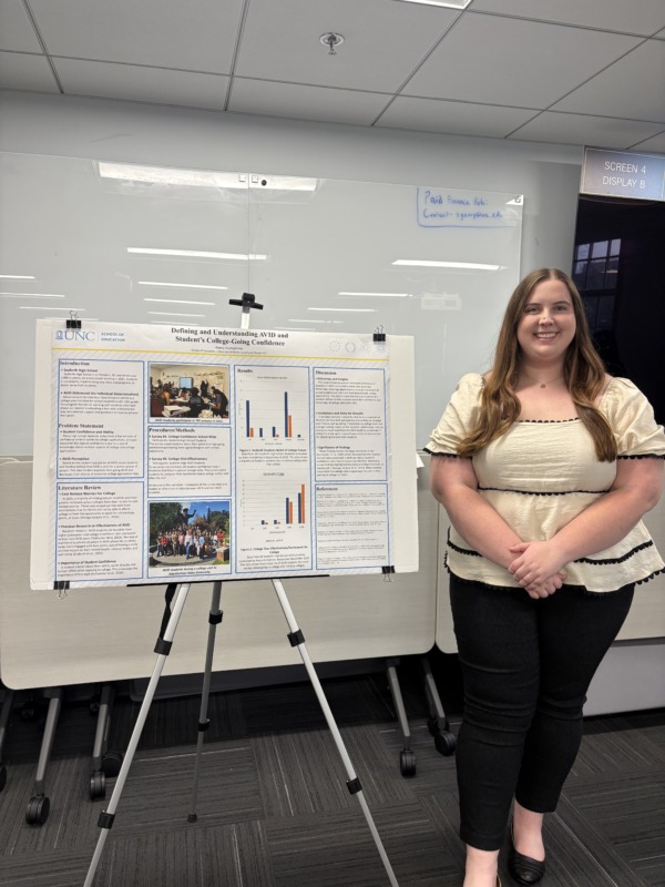 Avery Humphries stands beside her Human Development and Family Science research poster on AVID and student college-going confidence during a presentation event.