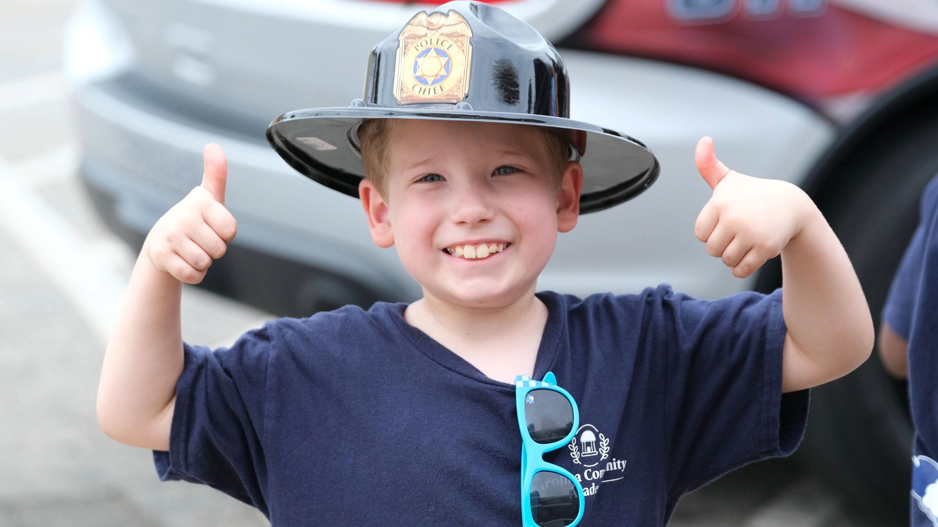 Smiling Carolina Community Academy student wearing a black police chief helmet gives two thumbs up while participating in a community partner activity during CCA’s inaugural summer camp.