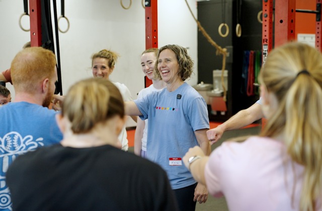 UNC School of Education faculty member Kara Hume stands smiling with a group of participants during an activity in a gym-like training space.