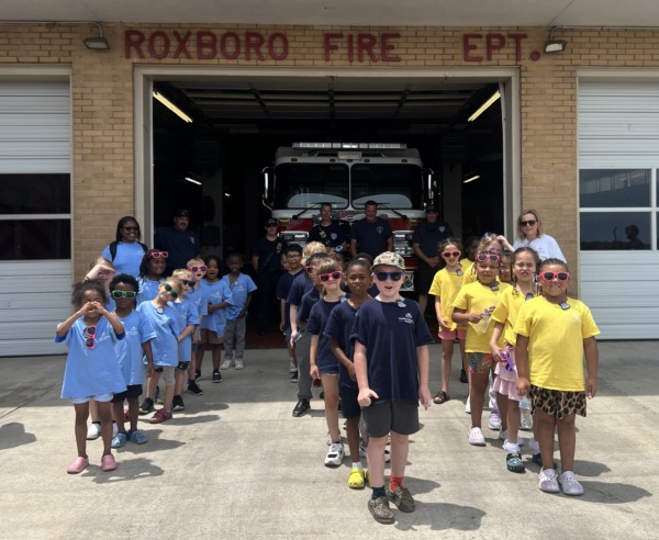 Carolina Community Academy students and staff stand outside the Roxboro Fire Department with firefighters and a fire truck behind them.