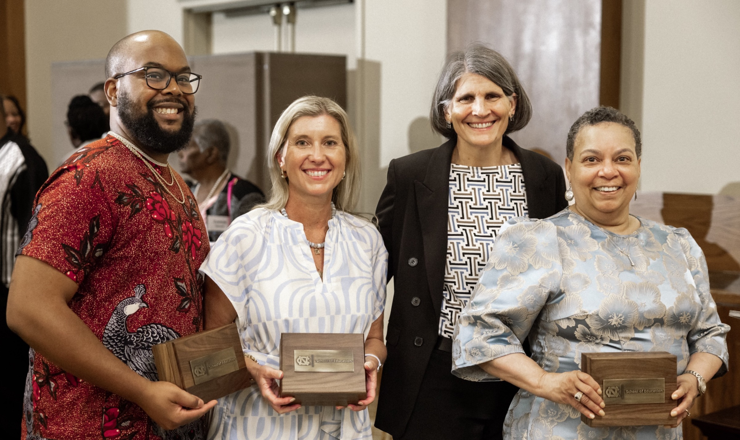 Four people smile for a group photo at the UNC School of Education Distinguished Alumni Awards ceremony, with three holding wooden award plaques.