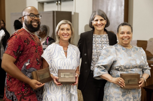 Four people smile for a group photo at the UNC School of Education Distinguished Alumni Awards ceremony, with three holding wooden award plaques.